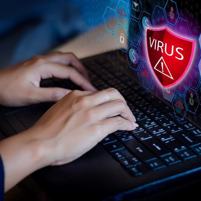 A woman working on the computer with a virus notification pop up on the screen.