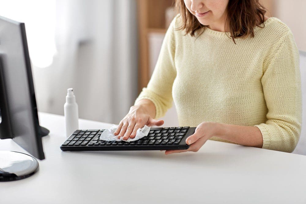 Woman wiping computer keyword with cleaning cloth.