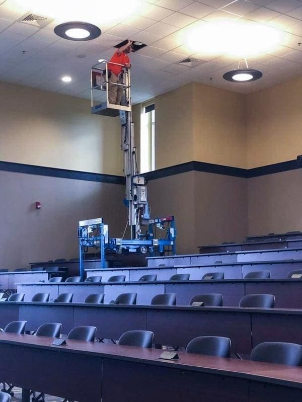 Worker on lift repairing ceiling in lecture hall.