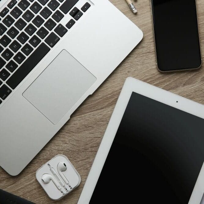 An Apple computer, iPhone, iPad, and headphones out on a wood table.
